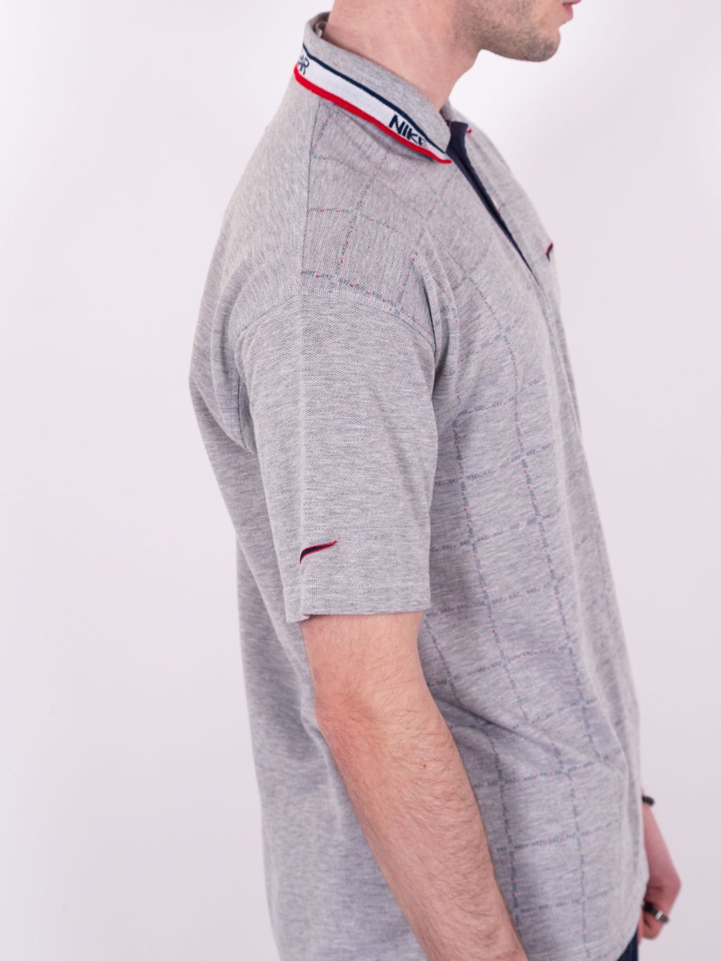 Polo Nike vintage des années 90 en gris avec quadrillage graphique, col liseré blanc sport wear, swoosh bicolore brodé et motif Nike répété - détail manche