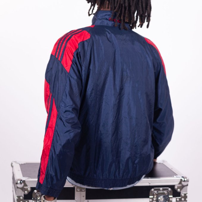 Veste Adidas vintage bleu marine avec bandes rouges sur les manches, coupe droite, col montant zippé, logo brodé sur la poitrine, style sportswear des années 90
