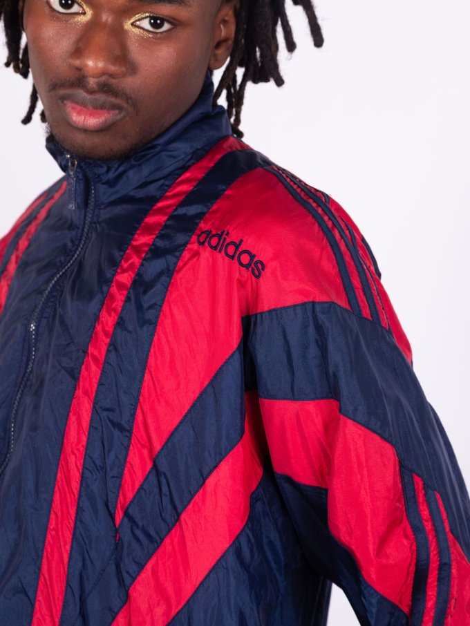 Veste Adidas vintage bleu marine avec bandes rouges sur les manches, coupe droite, col montant zippé, logo brodé sur la poitrine, style sportswear des années 90