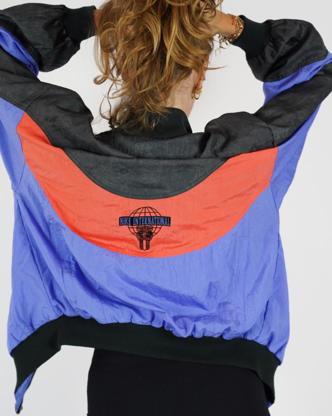 Veste vintage Nike International orange, bleu et noir avec logo brodé au dos.