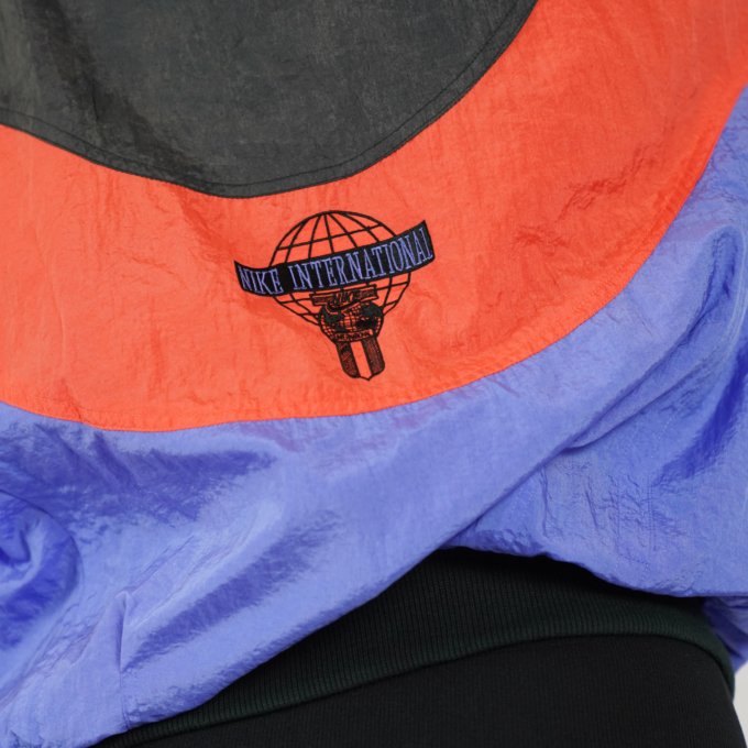 Veste vintage Nike International orange, bleu et noir avec logo brodé au dos.